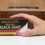 Hand holding a box of African Secret Black Soap in an office setting.