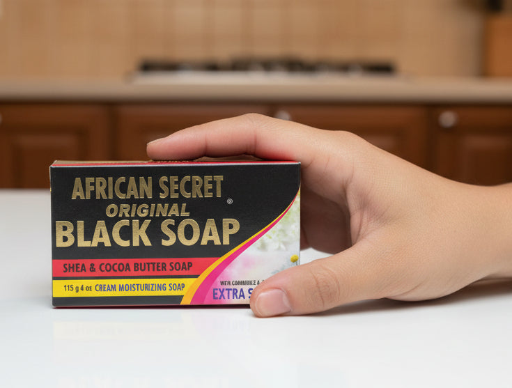 Hand holding a box of African Secret Black Soap in an office setting.
