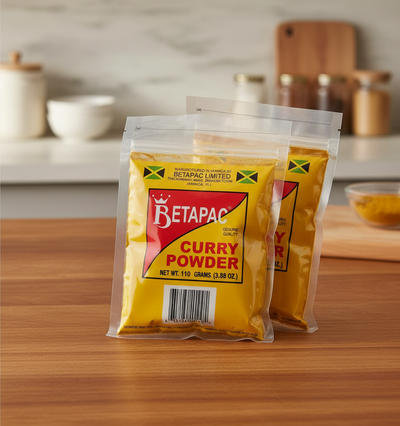 Two packages of Betapac Curry Powder, one in front and one behind, sealed in plastic, with yellow and red labeling and a green and red flag symbol.