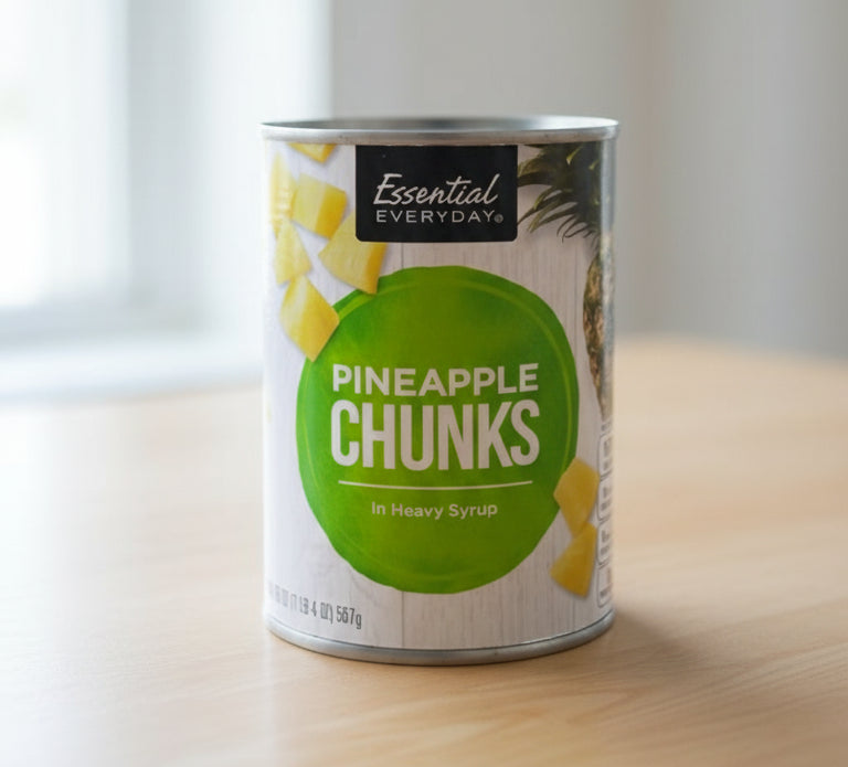 Can of Essential Everyday Pineapple Chunks in Heavy Syrup on a store shelf.