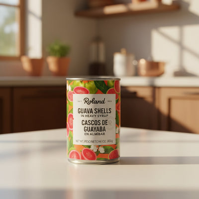 A can of Roland Guava Shells in Heavy Syrup, featuring a colorful label with illustrations of red guava and green leaves, resting on a dark desk.