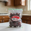 A clear plastic bag of Louis Fruit Preserves Spicy Red Plum, showing the dark red preserved fruit inside with a prominent red and white circular label on the front.