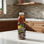A bottle of Caribbean Cool Mauby Drink on a plain white background. The bottle contains an amber-brown liquid and features a label with a palm tree, a yellow sun, and the brand name 'Caribbean Cool' in stylized lettering.